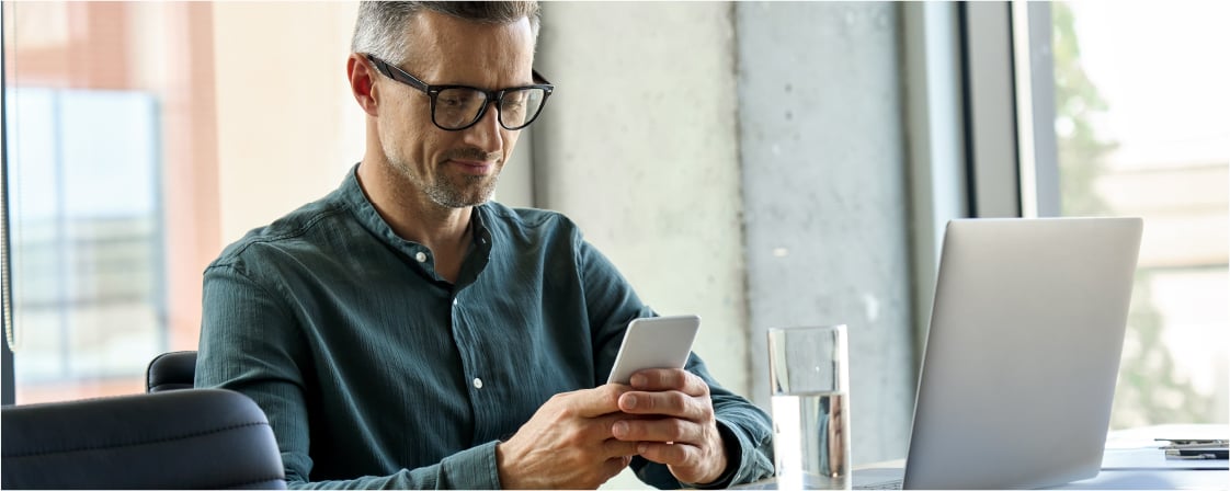 A white man with stylish glasses and business casual clothes works on his sales strategy on his cell phone.